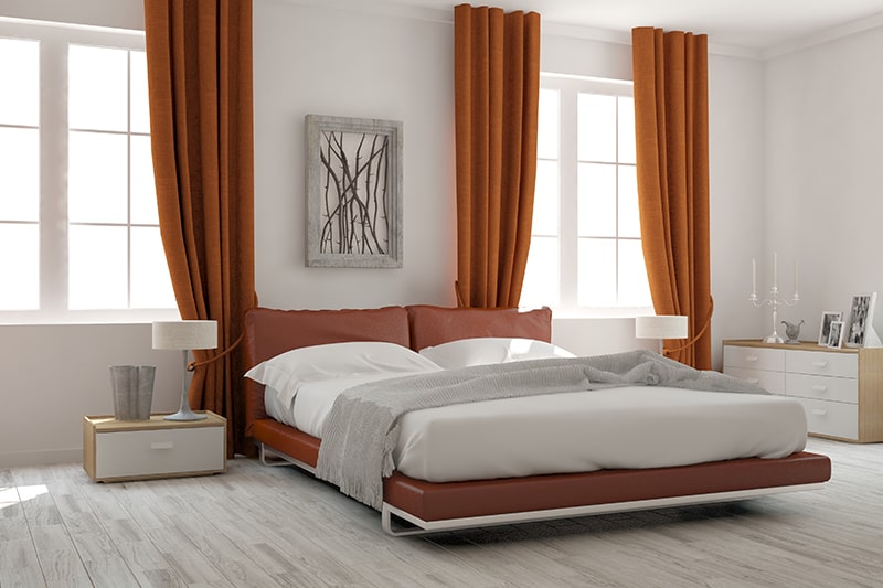 Bedroom designs india with a low lying bed frame against a pop of tangerine