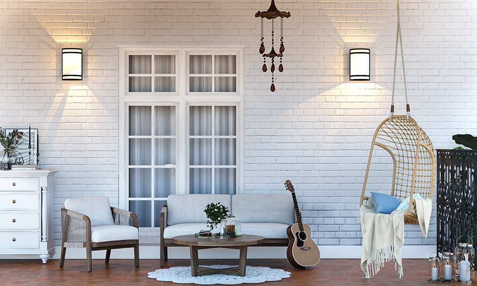 Home porch design with snow-white wall, sofa, wooden swing and an antique-looking wind chime