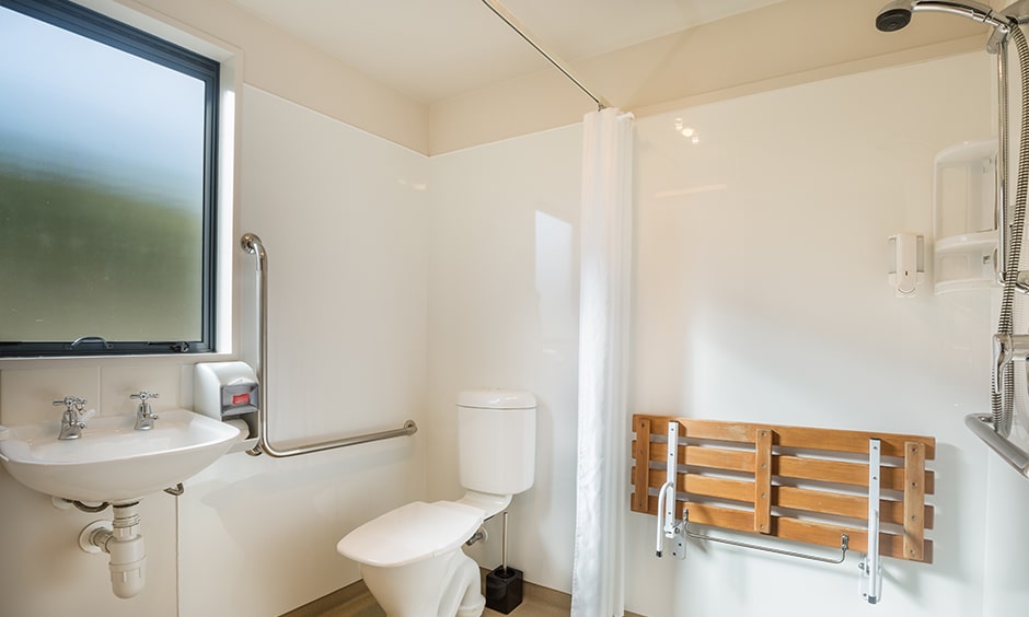 White bathroom design for senior citizens with a fold-up bench to take rest