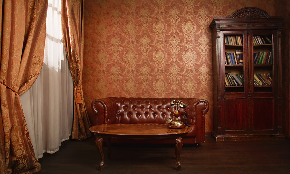 Brown gold wallpaper brings in old-world charm with elegant bookshelf and couch combined with other vintage furnishings