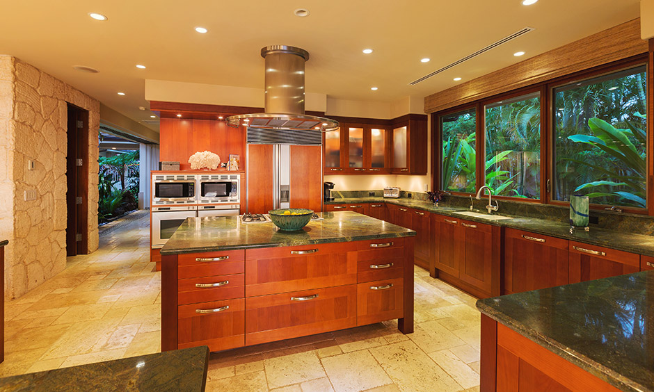 Luxury designer kitchens with wooden island & large windows with a view of trees outside give rustic rainfall feel.