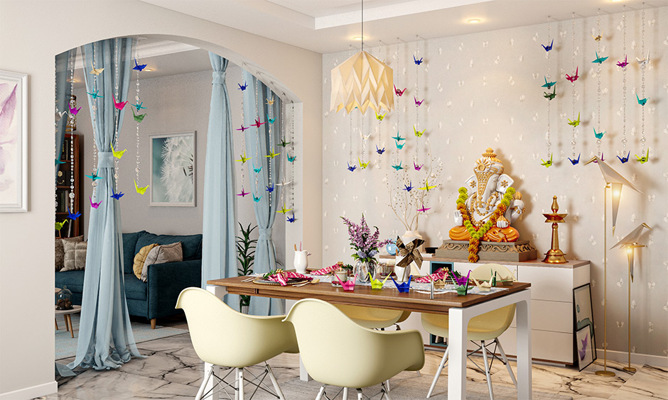 Ganpati decoration at home with origami in blues, yellows, and pinks colours & lights in this white room look beautiful.