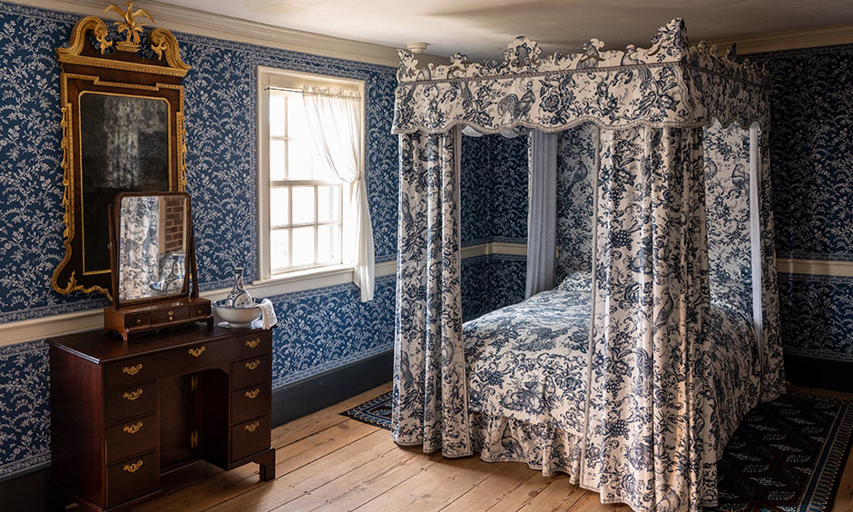 A four-poster bed design with matching curtains to a blue and white pattern bedroom wall