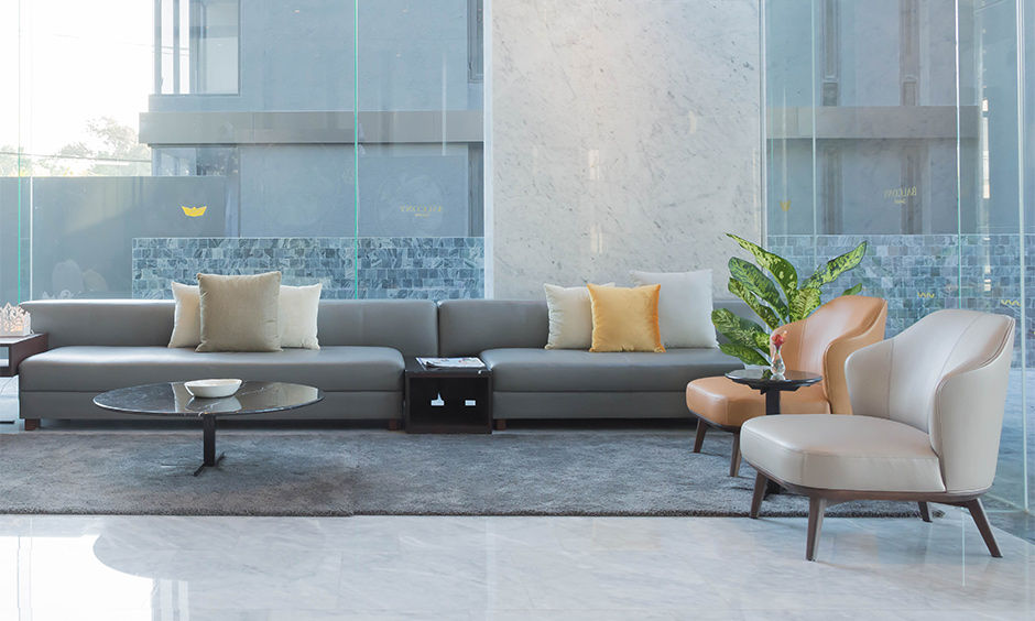 A lobby interior designed with a pop of colour, grey sofa and a tea table is elegant with a large glass window.