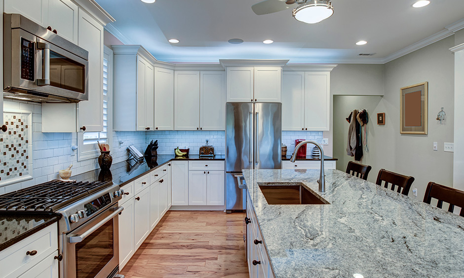 White granite countertops with a hint of grey in the white kitchen brighten and warm the hearts of your guests.