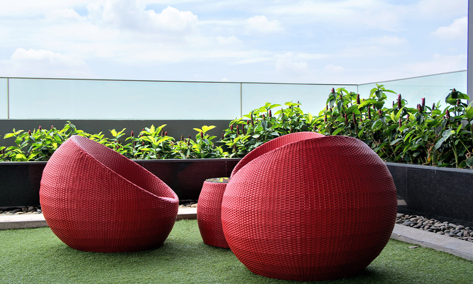 Apartment seating for balcony with red rattan spherical chairs and green turf on the floor brings some freshness.