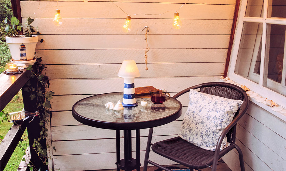 Balcony seating ideas with a wicker chair and frosted glass table and decorated with string light bulbs outdoor seating for small balcony.