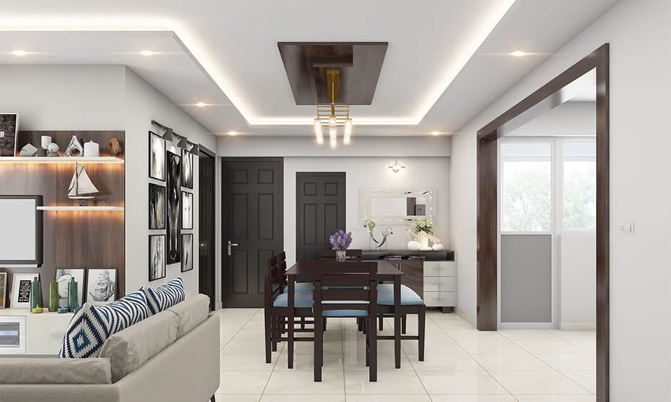 Living room cum dining hall ceiling designed in dark wood with cove and recessed lighting which brightens up the area.