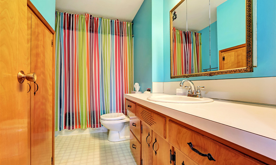 Light blue-toned kids bathroom ideas with brightly-striped shower curtains & lower wooden cabinets look fun and inviting.