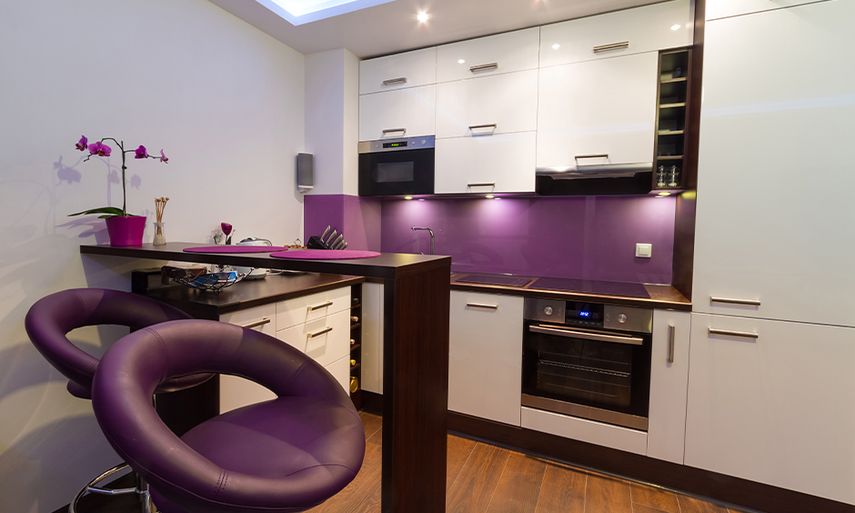 Backsplash coloured in purple and white kitchen with dining table and chairs in purple add vibrancy to space.