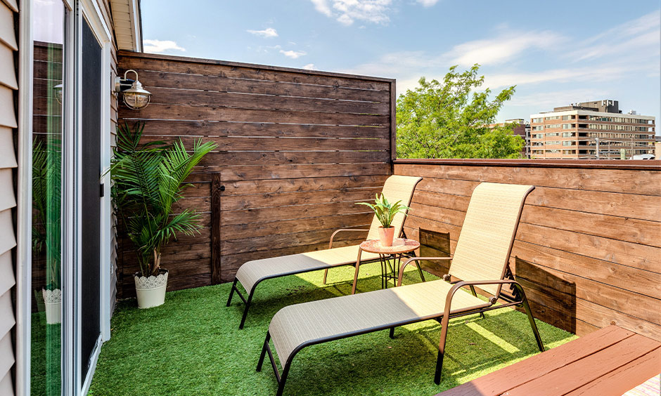 A pair of lawn chairs laid out on the green turf that is surrounded by the wooden walls is balcony seating design.