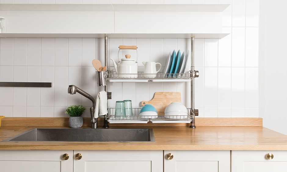 Over the kitchen sink shelf stainless steel segregated utensils in two-level to place plates, spoons and bowls.