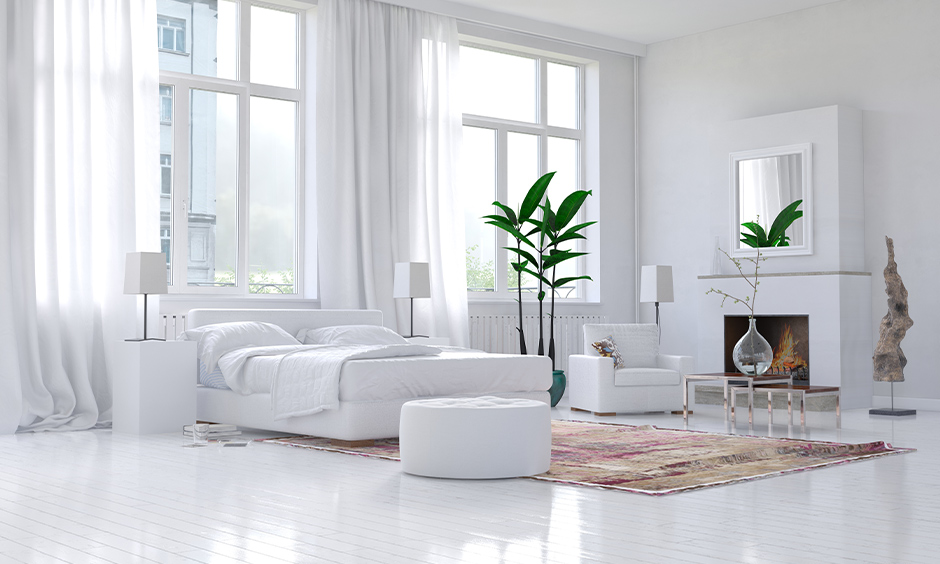 Large windows behind the bed and armchair in an all-white bedroom look stunning, Window design for bedroom Indian.