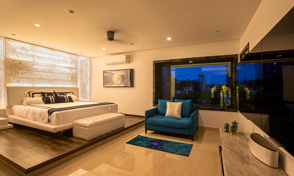 Master bedroom with a white bed, blue sofa and wall lighting behind the headboard, 4bhk independent house interior design.