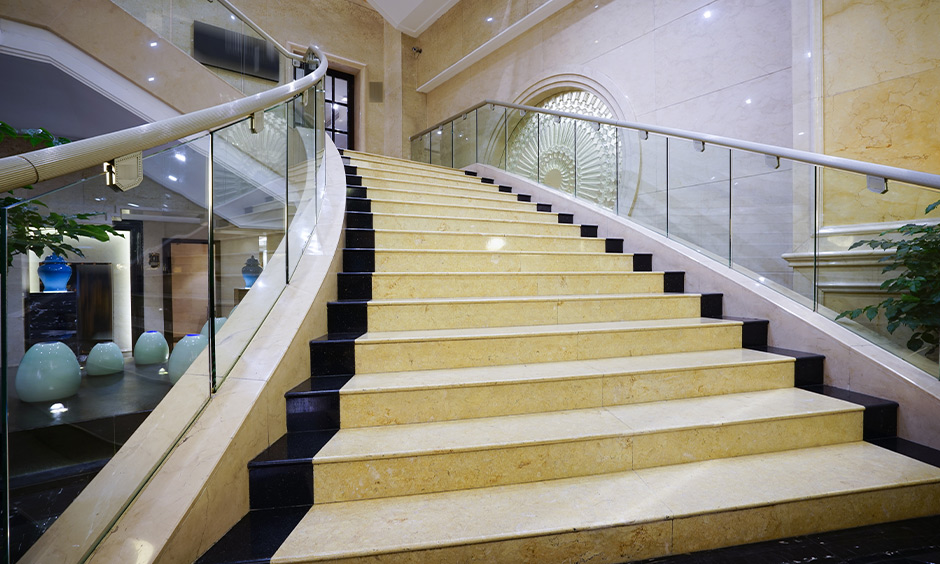 Dual-tone stair marble design in yellow and black with glass railing looks modern.