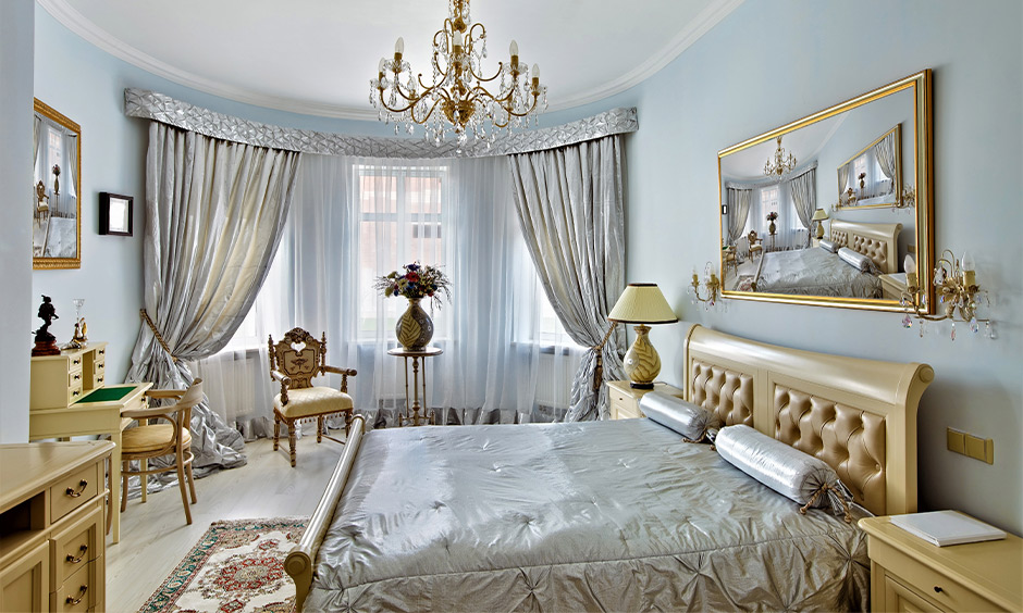 Soft blue bedroom in French country interior design with fancy drapes, study table, and chandelier brings airy vibe.