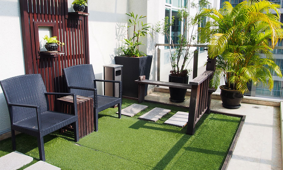 A small terrace with rattan chairs surrounded by potted plants and a patch of grass is a simple home garden idea.