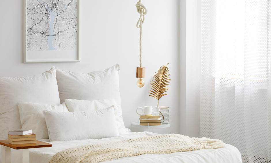 All-white bedroom with a rope hanging light in gold above the side table, and the transparent curtain is sleek.