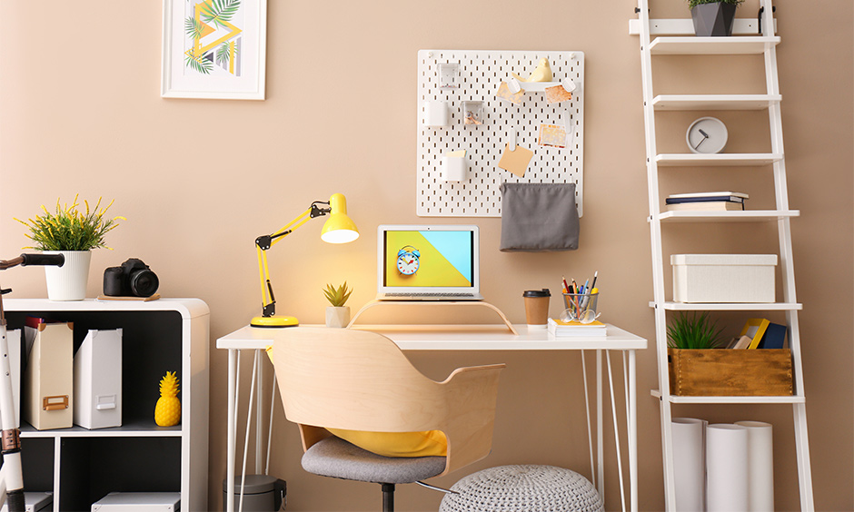 Creamy small study room decorating idea with table light, ladder shelf and notice board brings elegant look.