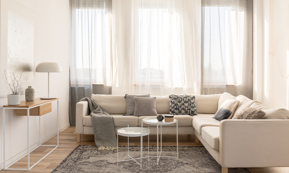 A white Scandinavian living room with a huge window and long floor curtains let in natural sunlight and a fresh vibe.