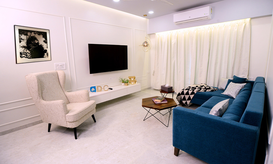 White minimalist living room for Indian apartment has an elegant moulding design with a royal blue sectional sofa.