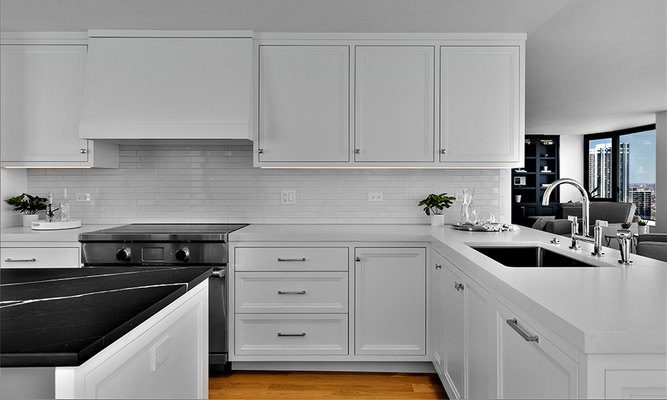 The black kitchen island countertop with white shaker style kitchen cabinets in glossy finish look pure and attractive.