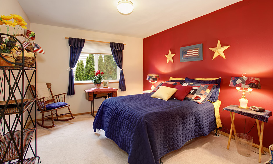 A small red bedroom wall with blue accent bed sheets and curtains adds character to space.