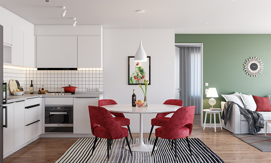 Open white kitchen cum dining area features red chairs and a white dining table.